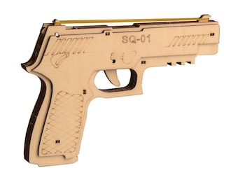 May include: A wooden toy gun with a rubber band, featuring the text "SQ-01". The toy gun is made of light-colored wood and has a detailed design, including a trigger and grip.