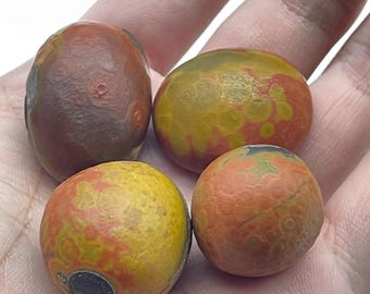 May include: Four rounded, polished stones with smooth surfaces. The stones display a variety of colors including deep brown, vibrant yellow, and orange, featuring intricate, circular, and mottled patterns across their surfaces.