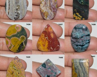May include: Assortment of ten colorful, polished, natural stone cabochons. The stones are in various shapes and sizes, including oval, teardrop, and rectangular. The colors include green, brown, red, yellow, and blue.
