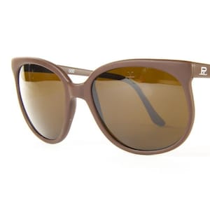 May include: Brown sunglasses with a rounded frame and brown lenses. The sunglasses have the text "VUARNET" printed on the right arm. The frame is a solid brown color.