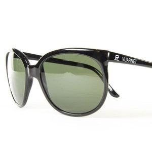 May include: Black sunglasses with green lenses. The sunglasses have a thick, rounded frame and the text "VUARNET" is printed on the right arm. The lenses are a dark green color, and the frame is glossy black.