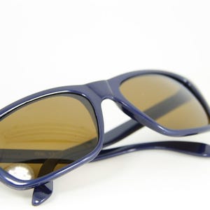 May include: A pair of blue sunglasses with brown lenses. The sunglasses are folded in half and the lenses are facing the camera.