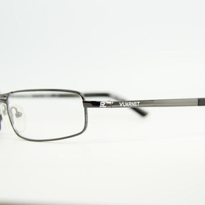 Könnte beinhalten: Eine Brille aus silberfarbenem Metall mit schwarzen Kunststoffbügeln. Der Markenname "VUARNET" ist auf dem rechten Bügel aufgedruckt.