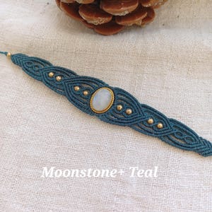 May include: Teal macrame bracelet with a moonstone gemstone and gold accents.  "Moonstone + Teal" is written below the bracelet.