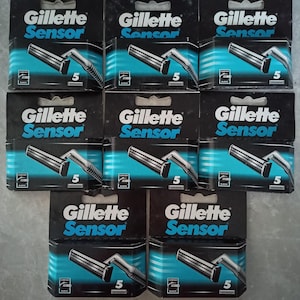 May include: A collection of Gillette Sensor razor blade refill packs. Each black and teal package displays the brand name and a graphic of the razor. The number "5" is visible on each package, indicating the number of blades.