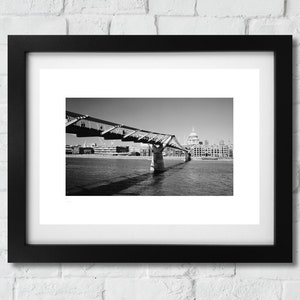 Puede incluir: Una fotografía en blanco y negro de un puente sobre un río con un edificio en el fondo.