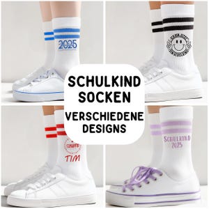 Könnte beinhalten: Weiße Socken mit blauen Streifen und der Zahl "2025" werden mit weißen Turnschuhen kombiniert. Andere Socken zeigen rote Streifen, ein Smiley und den Text "SCHULKIND". Das Bild zeigt verschiedene Socken-Designs.