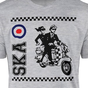 May include: A light gray t-shirt featuring a black and white graphic of a couple riding a scooter. The design includes a bullseye, checkered patterns, and the word "SKA" in bold letters. The shirt is a crew neck.