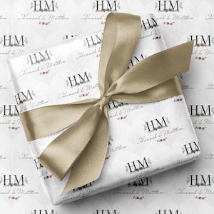 May include: A wrapped gift tied with a gold ribbon. The white wrapping paper features a repeating pattern of the initials "HM" and the names "Hannah & Matthew" in a decorative font. The background has a light grey diamond pattern.