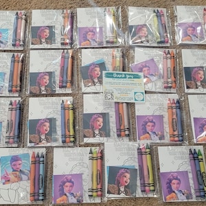 K&ouml;nnte beinhalten: Eine Sammlung von Buntstift-Sets, jeweils in durchsichtigem Kunststoff verpackt. Jedes Set enth&auml;lt eine Malvorlage mit einem Cartoon-Bild und dem Text "HAPPY 4TH BIRTHDAY CORAL". Die Sets sind auf einer braunen Oberfl&auml;che angeordnet.