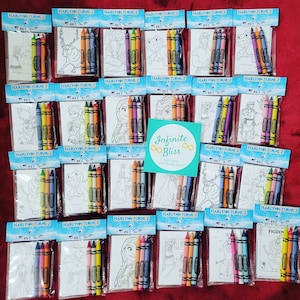 May include: A set of 20 Frozen-themed coloring pages and crayons packaged in clear plastic bags. Each bag has a blue and white label with the text "HARLYNN TURNS 2". The bags are arranged in rows on a red surface. The coloring pages feature characters from the movie Frozen, such as Elsa, Anna, Olaf, and Kristoff. The crayons are Crayola brand and come in a variety of colors.