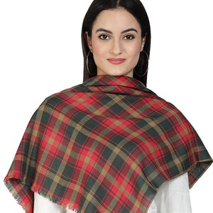 May include: A red, green, and brown plaid scarf with fringed edges. The scarf is draped around the shoulders of a person wearing a white long-sleeved shirt and blue jeans.