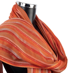 May include: A striped scarf in shades of orange, red, and brown. The scarf is draped over a mannequin's neck.