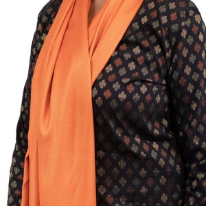 May include: A woman wearing a black and brown patterned long-sleeved shirt with an orange scarf draped around her neck.