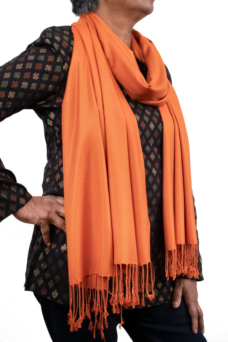 May include: A bright orange pashmina scarf with fringe. The scarf is draped around a person's neck and shoulders.