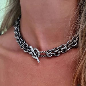 Può includere: Una collana a catena d'argento con chiusura a scatto. La catena è composta da due fili di metallo intrecciati.