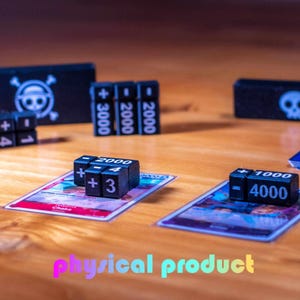 Può includere: Dadi neri con numeri e simboli bianchi sono disposti su una superficie di legno, accanto a carte da gioco. I dadi presentano segni più e meno e numeri come 1, 2, 3, 4, 2000, 3000 e 4000. L'immagine include anche scatole con teschi.