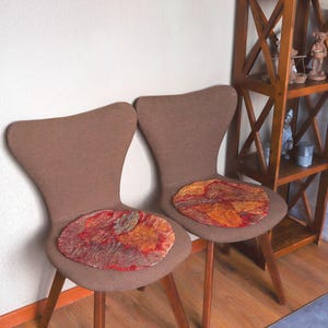 May include: Two brown chairs with wooden legs and red, orange, and gold patterned seat cushions.