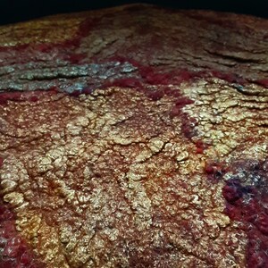 May include: Close-up of a textured, felted fabric with a red, gold, and white color scheme. The fabric has a unique, almost bubbly texture.