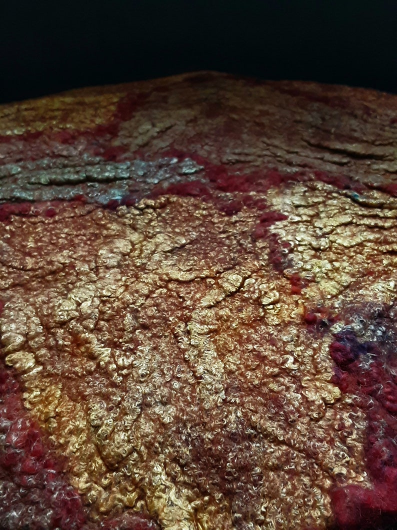 May include: Close-up of a textured, felted fabric with a red, gold, and white color scheme. The fabric has a unique, almost bubbly texture.