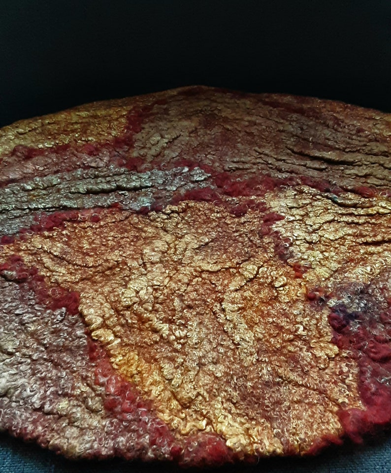May include: A round, felted wool rug with a textured surface. The rug is a mix of red, gold, and brown colors.