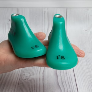 Könnte beinhalten: Zwei türkisfarbene Kunststoff-Schuhspanner, einer mit der Aufschrift "8" und der andere mit "8,5", werden in einer Hand gehalten.