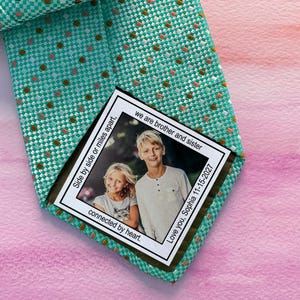 May include: A teal and brown patterned tie with a personalised photo label. The label includes a photo of two children and the text "we are brother and sister", "Side by side or miles apart, connected by heart", and "Love you, Sophia 11-15-2027".
