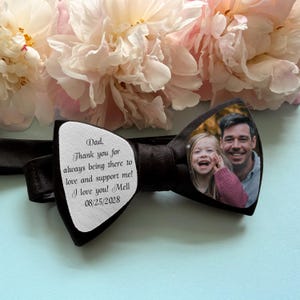Op de afbeelding: Een zwarte vlinderdas met een wit stoffen paneel bedrukt met de tekst: Dad, Thank you for always being there to love and support me! I love you! Mell 08/25/2028. De andere kant toont een kleurenfoto van een man en een jong kind.