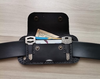 May include: Black leather belt pouch with a flap secured by two snaps. The pouch has two key holders and contains a bill and a card. The belt is black and has a rectangular shape.