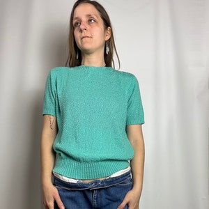 May include: A teal blue short-sleeved sweater with a ribbed hem.