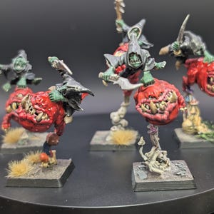 May include: Miniature fantasy figures of goblins riding red, bulbous creatures with large teeth. The goblins wear hooded cloaks and wield weapons. The figures are mounted on square bases with miniature scenery.