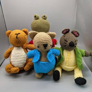 Könnte beinhalten: Vier gehäkelte Stofftiere: ein brauner Bär, eine braune Katze mit einer blauen Jacke, ein grüner Frosch und eine braune Maus mit einem gelben Hemd und einer grünen Jacke.