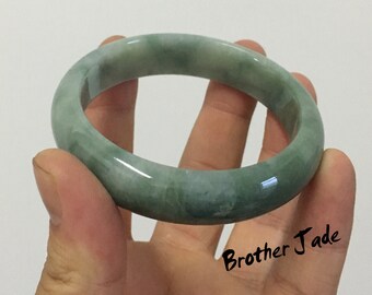 May include: A green jade bangle bracelet. The bracelet is smooth and polished, with a light green colour.