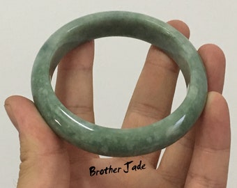 May include: A green jade bangle bracelet with a mottled pattern. The bracelet is smooth and polished.