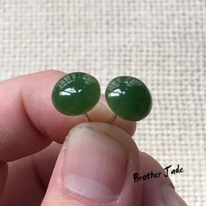 May include: A pair of green jade stud earrings with silver posts. The earrings are round and have a smooth, polished finish.