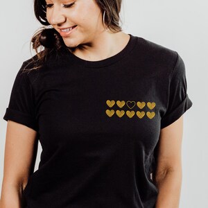 May include: Black t-shirt with a row of gold hearts, one of which is black.