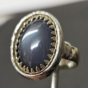 May include: A silver ring with a gray gemstone set in a decorative silver bezel. The bezel has a scalloped edge.