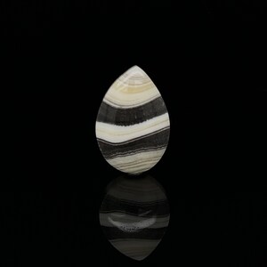 Puede incluir: Una piedra preciosa en cabuj&oacute;n en forma de l&aacute;grima con rayas blancas y negras. La piedra est&aacute; pulida y tiene una superficie lisa.