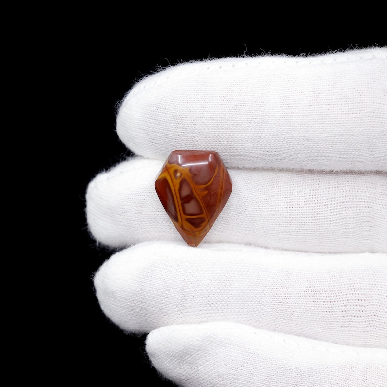May include: A red, orange, and white cabochon gemstone with a diamond shape. The gemstone has a swirling pattern.
