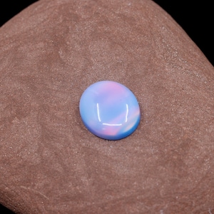 May include: A light blue and pink oval opal gemstone with a smooth, polished surface.