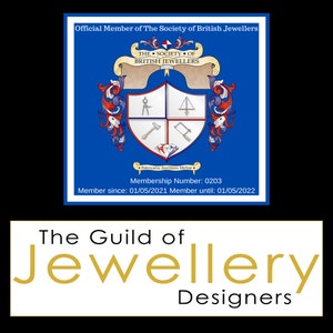 May include: A blue and white crest with the text "The Society of British Jewellers" and "Fabricatio Aurifices Melior". The crest includes a compass, a square, a hammer, a saw, and a diamond. The text "Membership Number: 0203" and "Member since: 01/05/2021 Member until: 01/05/2022" is below the crest. The text "The Guild of Jewellery Designers" is in gold letters on a white background.
