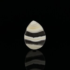 Puede incluir: Un cabuj&oacute;n en forma de l&aacute;grima con rayas blancas y negras. La piedra est&aacute; pulida y tiene una superficie lisa.