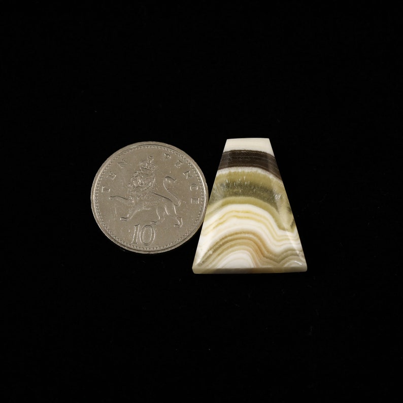 May include: A triangular cabochon of banded agate with white, brown, and green stripes. The stone is approximately the size of a US ten pence coin.