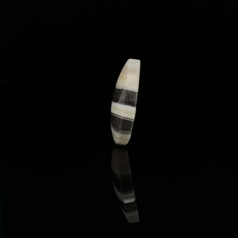 Puede incluir: Una cuenta de &aacute;gata rayada en blanco y negro con una forma ovalada y lisa.