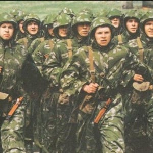 May include: A group of soldiers in camouflage uniforms and helmets marching in formation. They are carrying equipment and appear to be in a military exercise or training. The image has a vintage aesthetic.