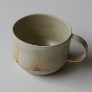 Peut inclure: Une tasse en céramique beige avec un glaçage brun et une anse arrondie.