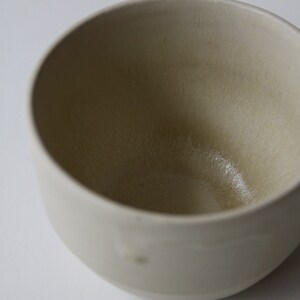 May include: A white ceramic bowl with a slightly textured surface. The bowl is empty and has a light beige color.