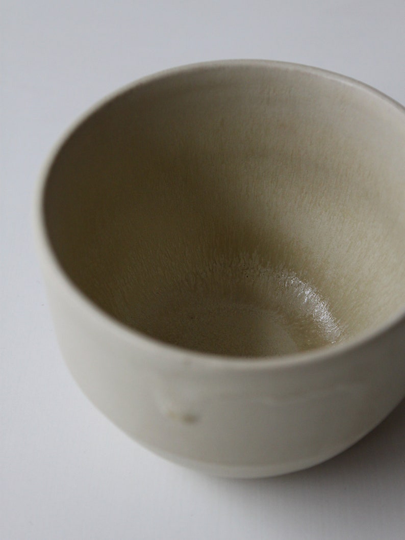 May include: A white ceramic bowl with a slightly textured surface. The bowl is empty and has a light beige color.