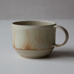 May include: A beige ceramic mug with a brown glaze and a rounded handle.