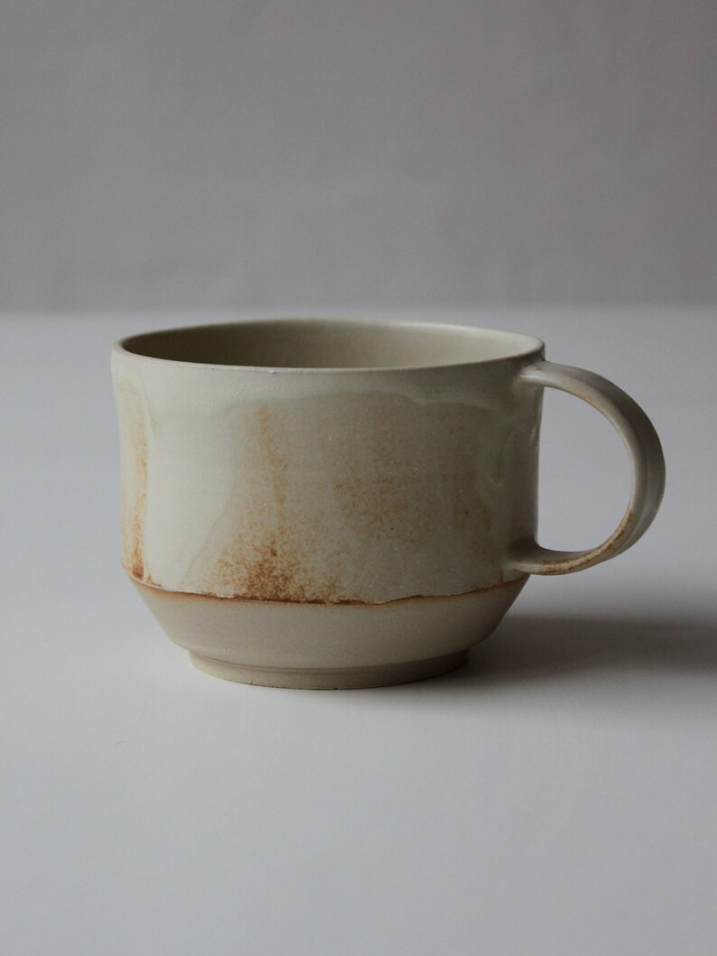 May include: A beige ceramic mug with a brown glaze and a rounded handle.